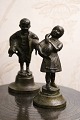 2 small 
decorative 
bronze figures 
of a boy with 2 
pigs under his 
arm and a girl 
holding a 
goose. ...