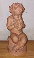 Terracotta 
figure 
depicting putti 
sitting on a 
stone eating 
grapes from 
grape cluster. 
Small ...