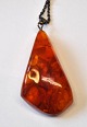 Large polished 
amber jewelery 
with seed 
capsules, 20th 
century. 
Length: 6 cm. 
With silver 
chain: ...