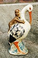 Piggy bank in the form of a cold-painted figure of a stork with a baby on its back. Appears with ...