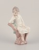 Lladro, Spain. Porcelain figurine of a girl sitting on a tree stump.Approximately from the ...