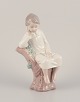 Lladro, Spain. 
Porcelain 
figurine of a 
girl sitting on 
a tree stump.
Approximately 
from the ...