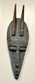 African mask, 
mid 20th 
century. Carved 
wood with 
beaten blue 
painted metal. 
With two horns. 
H.: ...