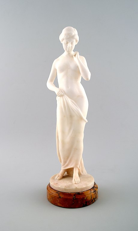 Stor figur af nøgen kvinde i alabast på marmor sokkel.
