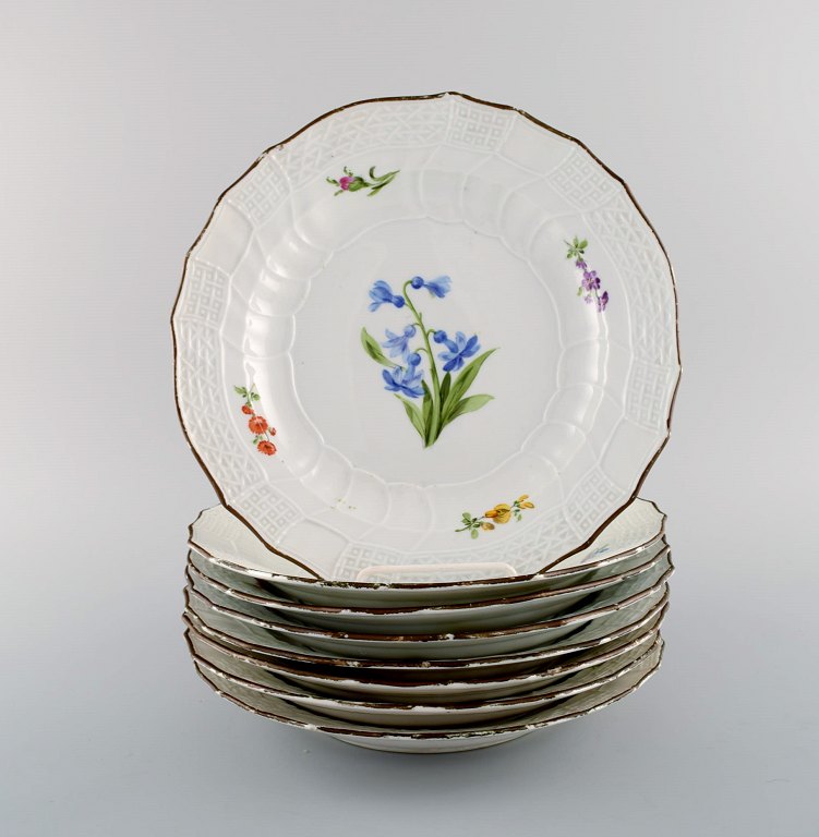 Otte antikke Meissen tallerkener i håndmalet porcelæn med blomstermotiver og 
guldkant. 1800-tallet.
