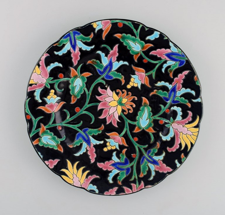 Longwy, Frankrig. Art deco tallerken i glaseret stentøj med håndmalede blomster 
og bladværk på sort baggrund. 1920/30