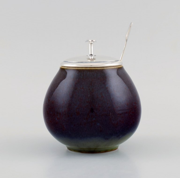 Royal Copenhagen and Franz Hingelberg. Lidded jar in glazed stoneware with 
modernist lid and spoon in sterling silver. Mid-20th century.
