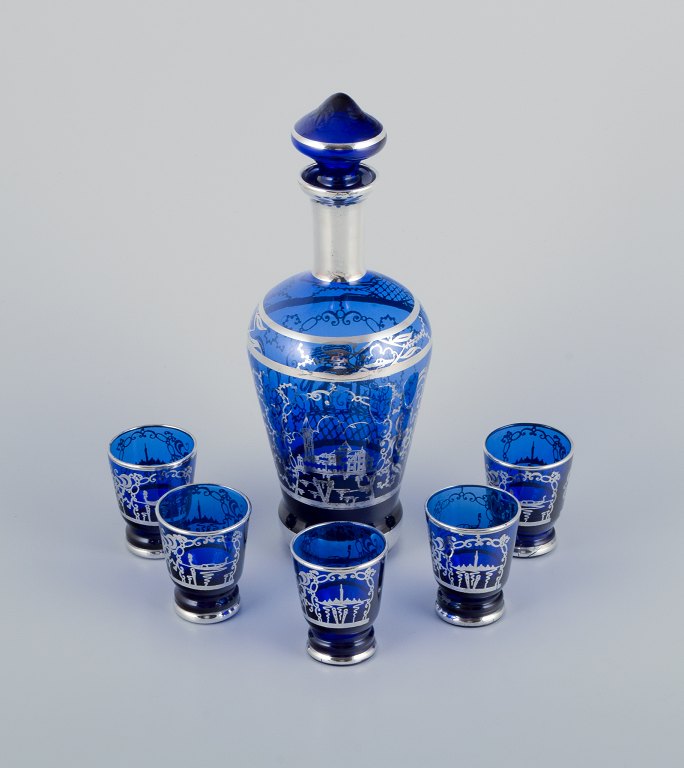 Venice, Italy. A liqueur set in blue glass consisting of a decanter and five 
cups. Hand-painted with silver decoration featuring Venice motifs.